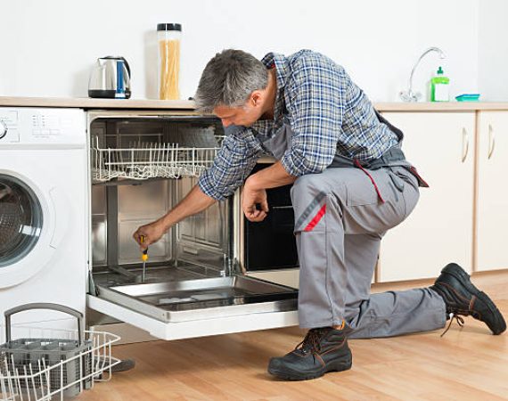Full length of repairman repairing dishwasher with screwdriver in kitchen